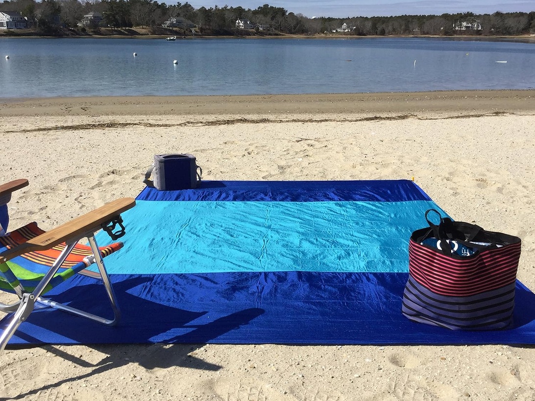 Een strandpicknick met een blauw kleed, een stoel, een koelbox en een tas op het zand.
